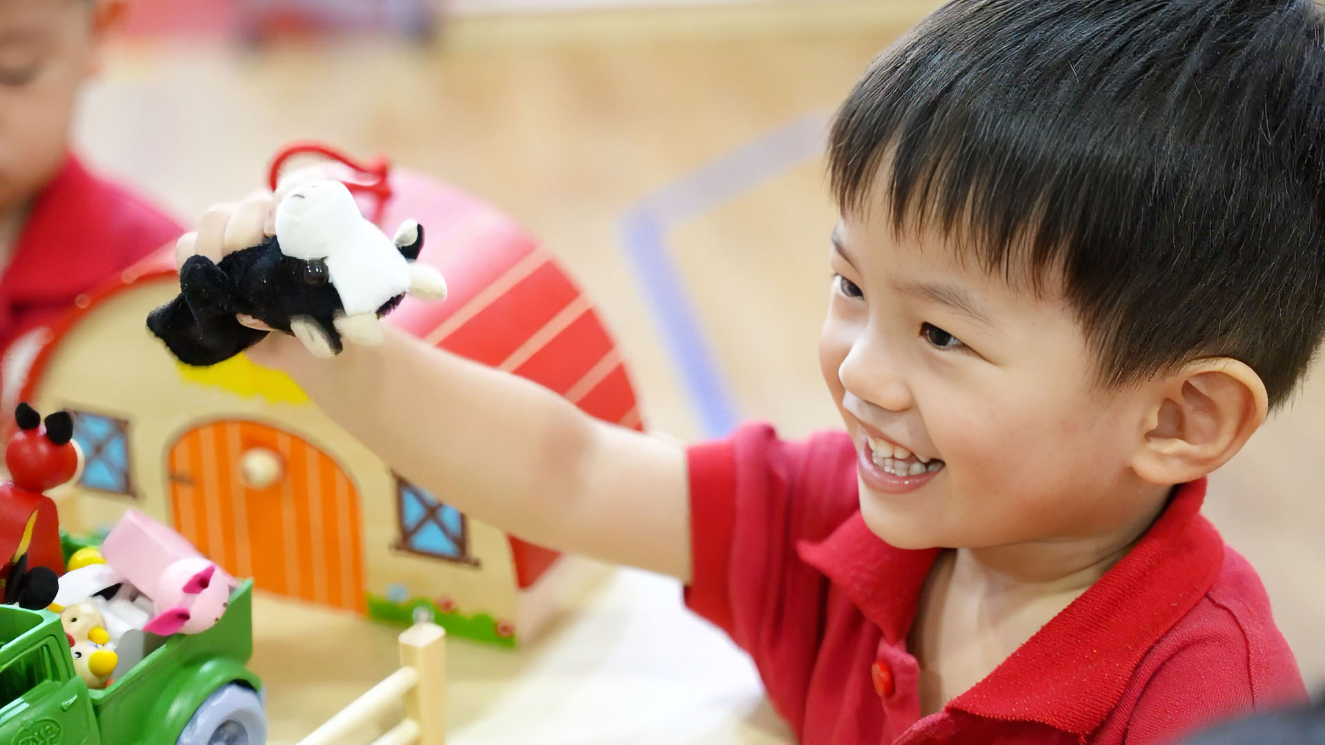 A child at MapleBear Jurong Gateway smiling while playing with a toy farm set